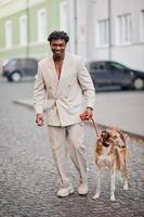 Stilvoller Afro-Mann im beigen Old-School-Anzug mit russischem Barsoi-Hund. Modischer junger afrikanischer Mann in Freizeitjacke auf nacktem Oberkörper. foto