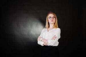 Studioporträt einer blonden Geschäftsfrau mit Brille, weißer Bluse und schwarzem Rock vor dunklem Hintergrund. erfolgreiche frau und stilvolles mädchenkonzept. foto