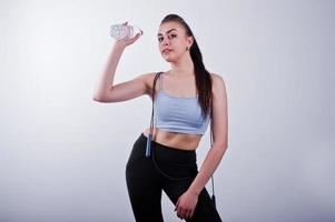 Fröhliche attraktive junge Fitness-Frau in Top und schwarzen Leggings mit Springseil und Flasche Wasser isoliert auf weißem Hintergrund. foto