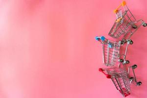 Minimales Online-Shopping-Konzept, bunte Papiereinkaufstasche und Trolley gehen von schwebendem rosa Hintergrund für Kopierraum herunter. Der Kunde kann alles von zu Hause kaufen und der Bote liefert. foto