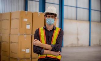 werksingenieur wird inspiziert und überprüft den qualitätsproduktionsprozess auf der herstellungsstation für gesichtsmasken, indem er auf der fabrikplantage eine lässige uniform und einen schutzhelm trägt. foto