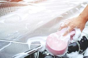 menschen mann hält hand rosa schwamm zum waschen des autos. Radreifen reinigen. konzept autowäsche sauber. foto