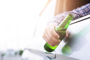 Nahaufnahme handbetrunkener junger Mann beim Autofahren mit einer Flasche Bier. trinken und fahren sie kein konzept. Fahren in betrunkenem Zustand kann die Gefahr eines Todes sein. foto