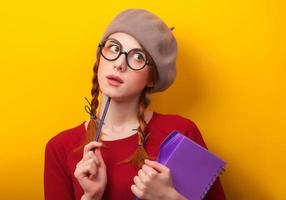 rothaariges Mädchen mit Notizbuch und Bleistift auf gelbem Hintergrund. foto