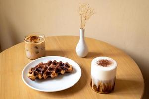 ein sonntagsmorgenessen im café, zwei tassen kaffee, honiglatte und eispanner americano, serviert mit waffel auf teller, dekoriert mit mit vase. foto