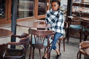 afrikanische frau im karierten kap stellte caféterrasse im freien mit handy auf. foto