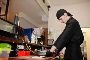 professionelle kochkleidung in schwarz, die sushi und brötchen in einer restaurantküche mit japanischer traditioneller küche herstellt. foto