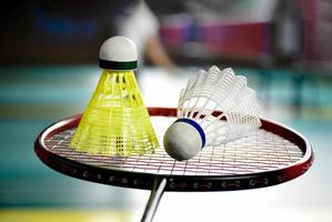 Weißer und gelber Badmintonfederball aus Kunststoff und Schläger mit Neonlichtschattierung auf grünem Boden im Indoor-Badmintonplatz, verschwommener Badmintonhintergrund, Kopierraum. foto