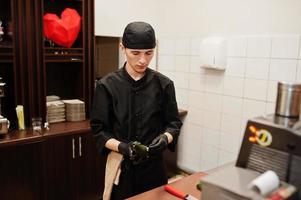 professionelle kochkleidung in schwarz, die sushi und brötchen in einer restaurantküche mit japanischer traditioneller küche herstellt. foto