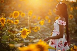 hübsche junge schwarze Frau tragen Sommerkleid Pose in einem Sonnenblumenfeld. foto