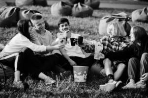 junge multiethnische gruppe von menschen, die filme im poof im open-air-kino ansehen und trinken. foto