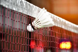 Cremeweißer Badmintonfederball und Schläger mit Neonlichtschattierung auf grünem Boden im Indoor-Badmintonplatz, verschwommener Badmintonhintergrund, Kopierraum. foto