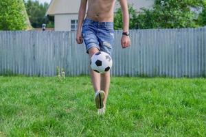 Junger Mann in Jeans und weißen Turnschuhen, der draußen Fußball spielt. Amateur-Fußballer prägt den Ball foto