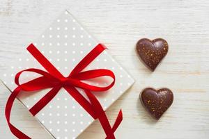grußkarte zum valentinstag. Schokoladenbonbons in Herzform und Geschenkbox mit rotem Festband auf Holzhintergrund foto