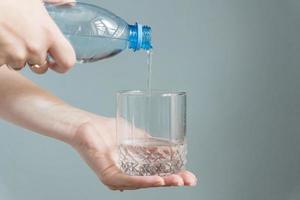 Frau gießt Wasser in ein Glas auf grauem Hintergrund foto