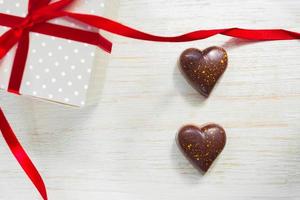 grußkarte zum valentinstag. Schokoladenbonbons in Herzform und Geschenkbox mit rotem Festband auf Holzhintergrund foto