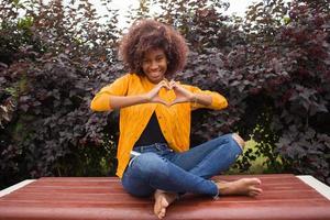 eine glückliche und junge afroamerikanerin zeigt mit ihren händen ein herz foto