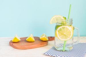 Zitruslimonadenwasser mit geschnittener Zitrone und Minze, gesundes und entgiftendes Wassergetränk im Sommer auf Holztisch mit blauem hellem Hintergrund foto