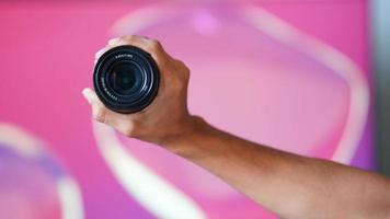 kameraobjektiv, das in der hand mit rosa hintergrund hält. foto