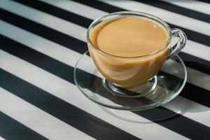 transparente tasse cremiger kaffee auf dunklem hintergrund. Sonnenlicht und harte Schatten. getöntes bild mit kopienraum foto