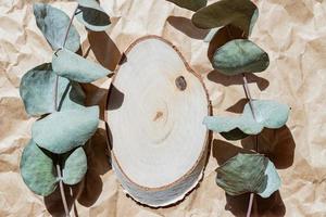 Draufsicht auf leeren Holzschnitt mit Eukalyptusblättern auf Papierhandwerkshintergrund. Mockup-Präsentation für Waren oder Kosmetika. Nahansicht foto