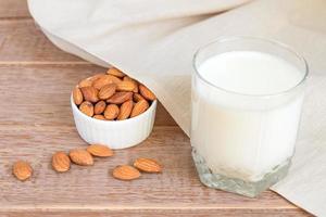 Hausgemachte Mandelmilch in einem Glas und Nüssen in weißer Porzellanschüssel auf Holzhintergrund foto