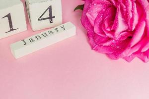 valentinstag- und feiertagskonzept - nahaufnahme des holzkalenders mit dem datum vom 14. februar und rosa rose mit wassertropfen auf rosa hintergrund foto