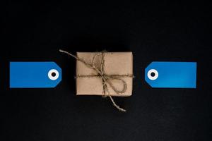 handgefertigte geschenkbox in kraftpapier eingewickelt mit blauen papierkartenanhängern zur dekoration. foto