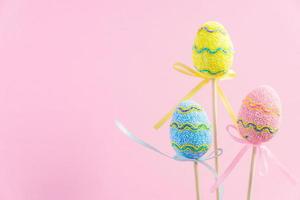 Ostern lila, gelb und blau dekorierte Eier stehen auf Holzstäbchen auf rosa Hintergrund. minimales osterkonzept. frohe osterkarte mit kopierraum für text. foto