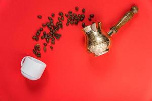 Draufsicht auf Kaffeebohnen in Cezve traditionelle türkische Kaffeekanne, weiße Tasse auf rotem Hintergrund. foto