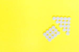 weiße Medizinpillen in Form eines Pfeils auf gelbem Hintergrund. medizinisches und gesundheitskonzept foto
