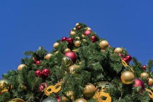 weihnachts- und neujahrsferienhintergrund. weihnachtsbaum geschmückt mit kugeln und girlanden gegen blauen himmel, unteransicht foto