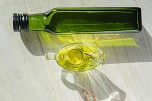 Sauciere aus Glas mit extra nativem Olivenöl und grüner Flasche auf Holztisch. foto