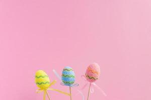 Ostern lila, gelb und blau dekorierte Eier stehen auf Holzstäbchen auf rosa Hintergrund. minimales osterkonzept. frohe osterkarte mit kopierraum für text. foto