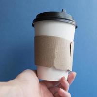 Weißer Kraftpapier-Einwegbecher für Kaffee mit schwarzem Kunststoffdeckel. Kaffee zum Mitnehmen auf blauem Hintergrund. foto