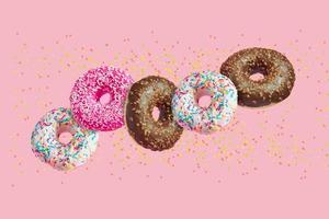 glasierte donuts in bewegung, die auf rosa hintergrund mit bunten streuseln fallen foto