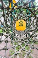 Innenansicht eines langen Seilmaschenrohrs, am Ende des Tunnels gelber Spielplatz unscharfer Hintergrund foto