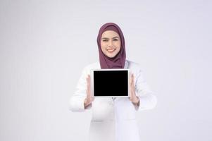 schöne muslimische geschäftsfrau im weißen anzug mit hijab, der tablette im studio hält foto