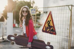 Mädchen in einer roten Jacke mit einem Skateboard foto