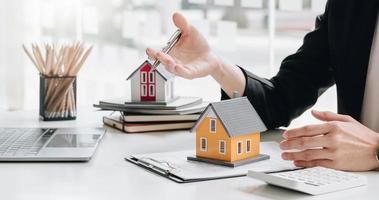 Immobilienmakler-Agent präsentiert und berät den Kunden bei der Entscheidungsfindung, unterzeichnet einen Versicherungsvertrag, kauft und verkauft ein Hausmodell, ein Hypothekendarlehensangebot für und eine Hausversicherung foto