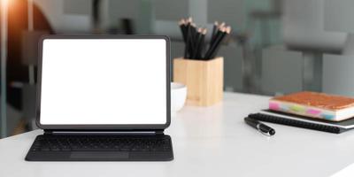 mockup-tablet mit leerem bildschirm und magischer tastatur auf holztisch im büro. foto