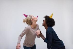 lächelnde frauen in partykappen, die zu pfeifen blasen foto