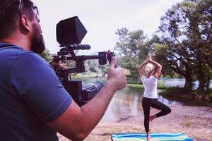 junger Videofilmer, der aufnimmt, während eine Frau Yoga-Übungen macht foto