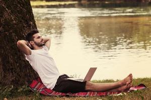 Mann mit einem Laptop am Ufer des Flusses foto