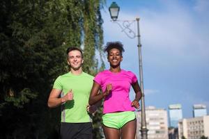 Junges lächelndes multiethnisches Paar, das in der Stadt joggt foto