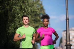 Junges lächelndes multiethnisches Paar, das in der Stadt joggt foto