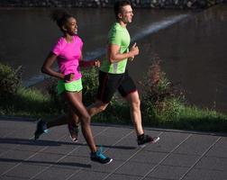 Junges lächelndes multiethnisches Paar, das in der Stadt joggt foto