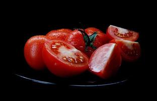 in Scheiben geschnittene rote Tomaten auf einem schwarzen Teller sind auf schwarzem Hintergrund isoliert. Beschneidungspfad. foto