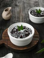 Bubur Ketan Hitam, indonesischer Nachtisch. Schwarzer Klebreisbrei mit Kokosmilch, Zucker und Pandanblatt. serviert in einer weißen Schüssel auf einem Holztisch. foto