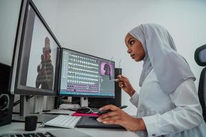 Junge afroamerikanische moderne muslimische Geschäftsfrau mit Schal an einem kreativen, hellen Büroarbeitsplatz mit großem Bildschirm. foto
